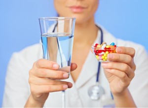 девушка держит стакан воды и таблетки
